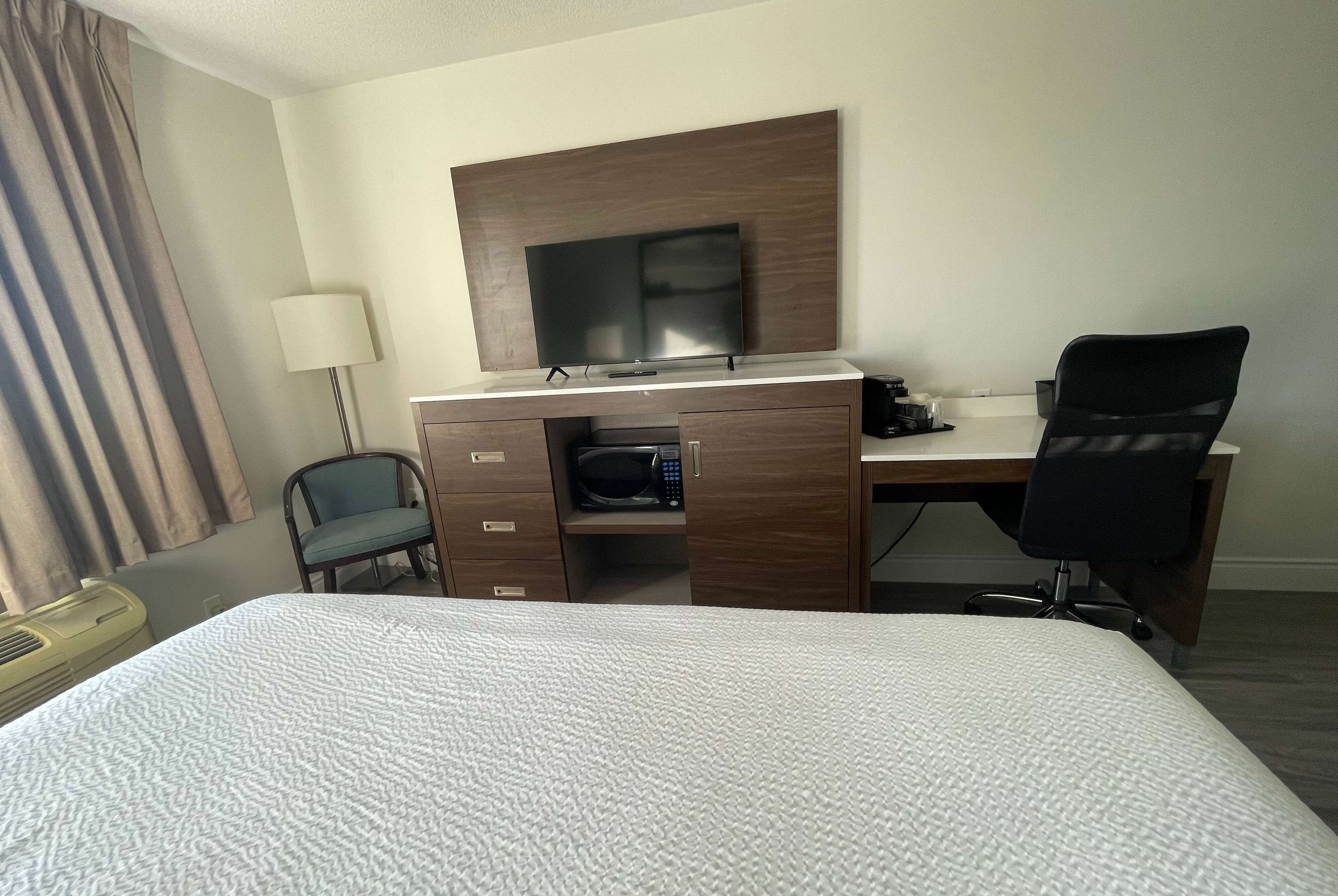A hotel room with a bed, a desk with a flat-screen TV, a chair, a lamp, and a microwave.