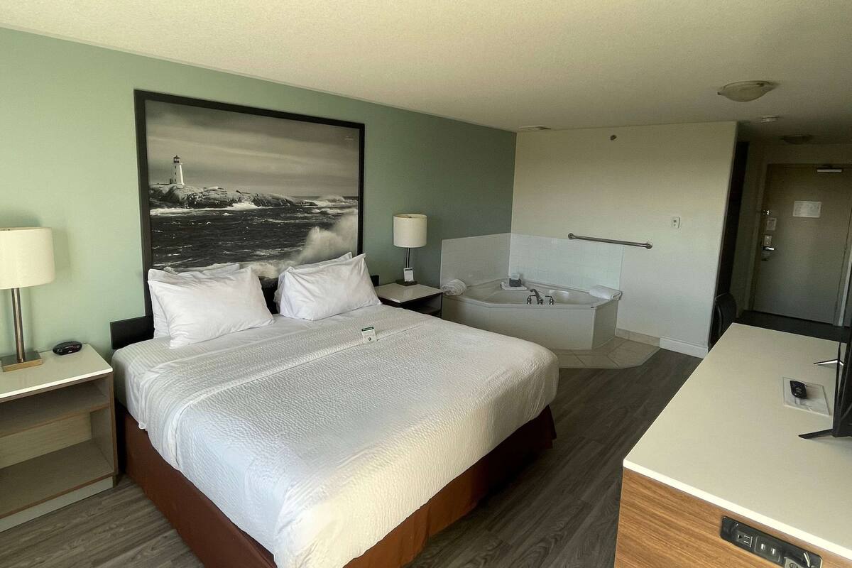 Habitación de hotel con cama, mesita de noche, escritorio, baño con bañera y un cuadro grande de un faro en la pared.