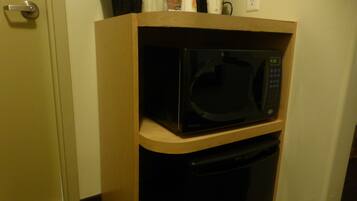 Un four à micro-ondes compact, posé sur une étagère en bois dans un petit coin cuisine.