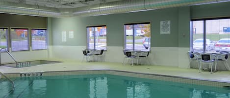 An indoor swimming pool with clear safety markings, windows with blinds, and a caution sign on the wall.