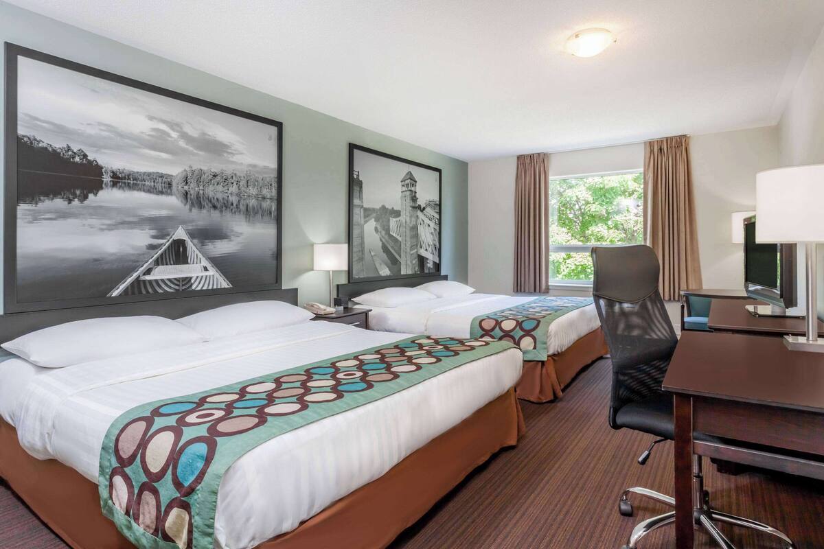 Habitación de hotel con dos camas, un escritorio, una silla y un ventanal grande.