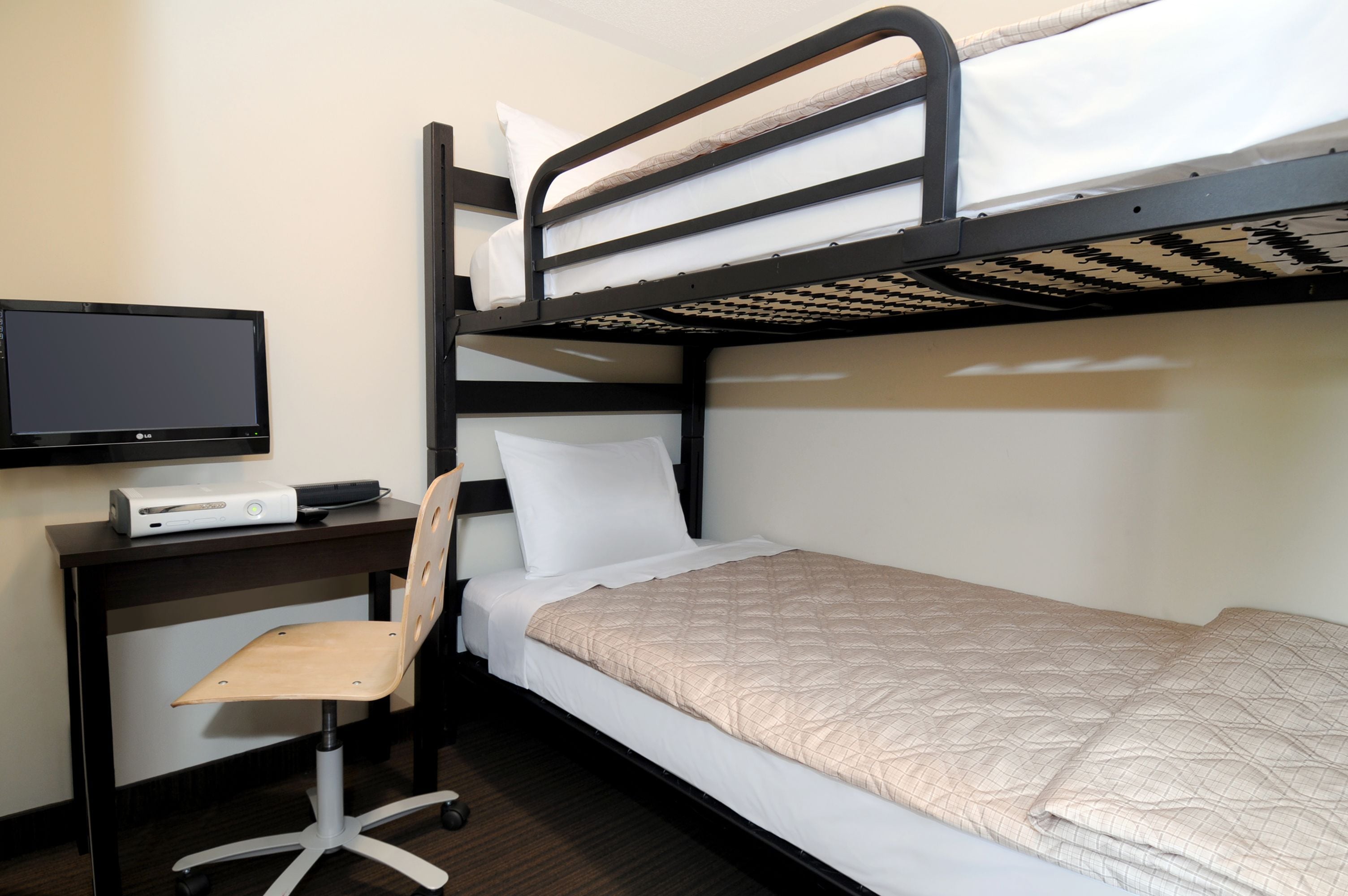A bunk bed with a TV and desk, a chair, and a bed with a quilted cover.