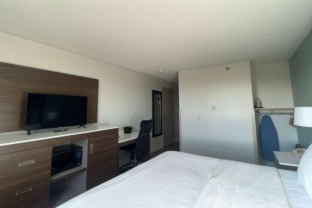 Una habitación de hotel con cama, escritorio, televisor de pantalla plana, microondas, silla y armario.
