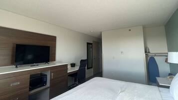 A hotel room with a bed, a desk with a flat-screen TV, a microwave, a chair, and a wardrobe.