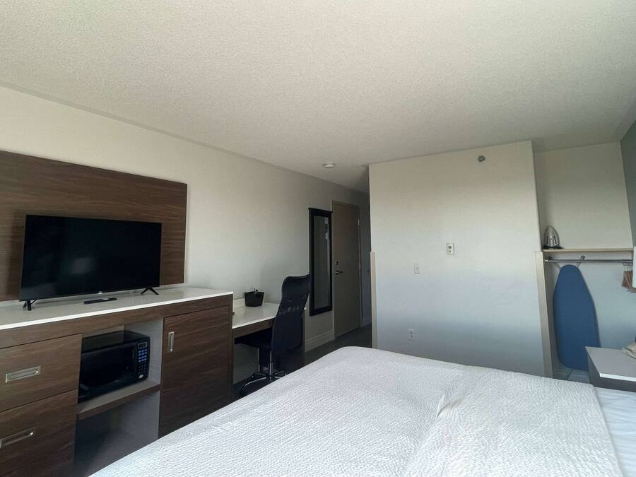 A hotel room with a bed, a desk with a flat-screen TV, a microwave, a chair, and a wardrobe.
