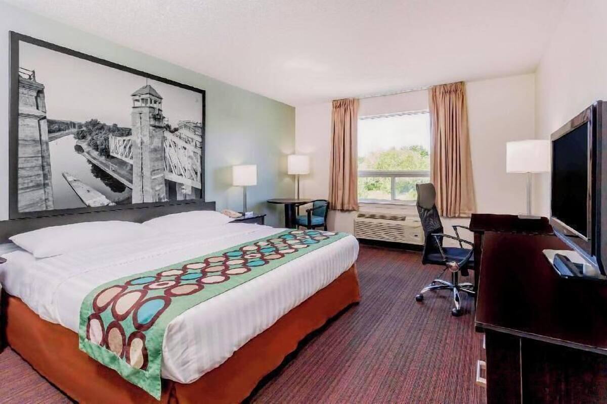 Una habitación de hotel con una cama grande, un escritorio, un televisor y una ventana con cortinas.