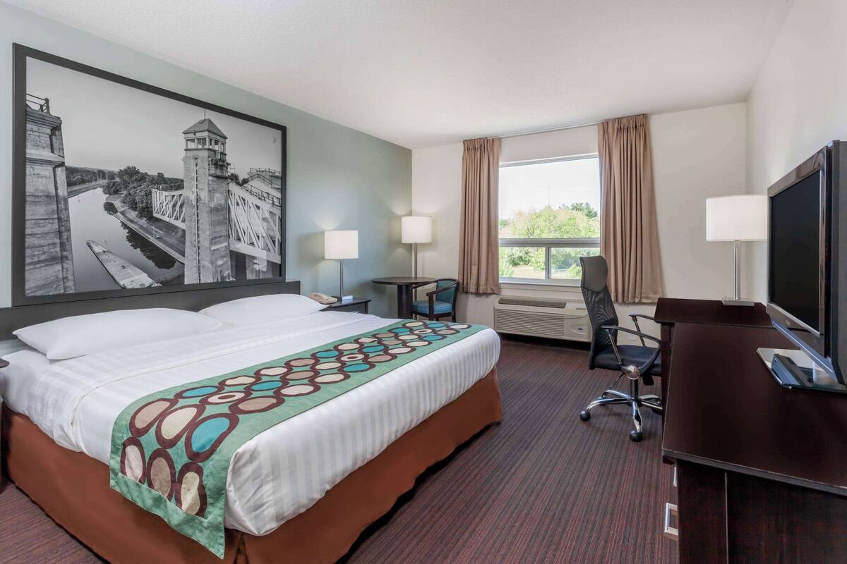 Habitación de hotel con una cama grande, un escritorio, una silla, un televisor y una ventana con cortinas.