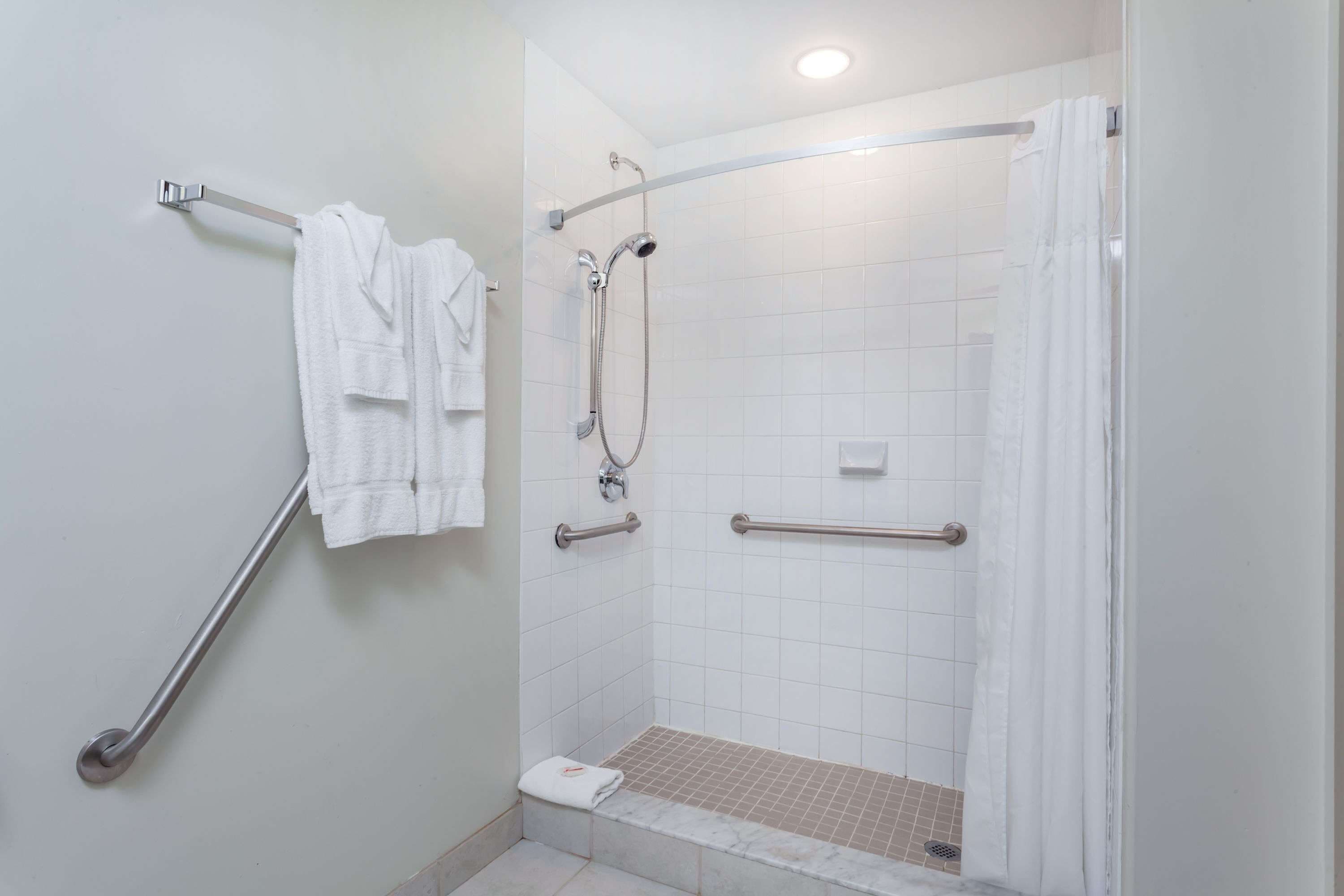 A bathroom with a walk-in shower, grab bars, and a towel rack.