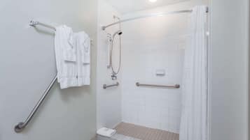 A bathroom with a walk-in shower, grab bars, and a towel rack.