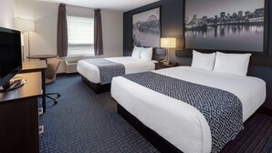 Ein Hotelzimmer mit zwei Betten, einem Schreibtisch, einem Sessel, einem Fernseher und einem Stadtbild an der Wand.
