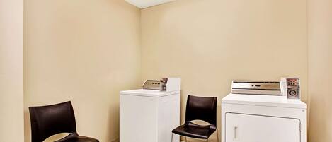 A laundry room with two washing machines and two chairs.