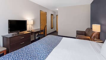 Une chambre d’hôtel comprenant un lit, un bureau avec une télévision, une chaise, un fauteuil en cuir et une lampe.