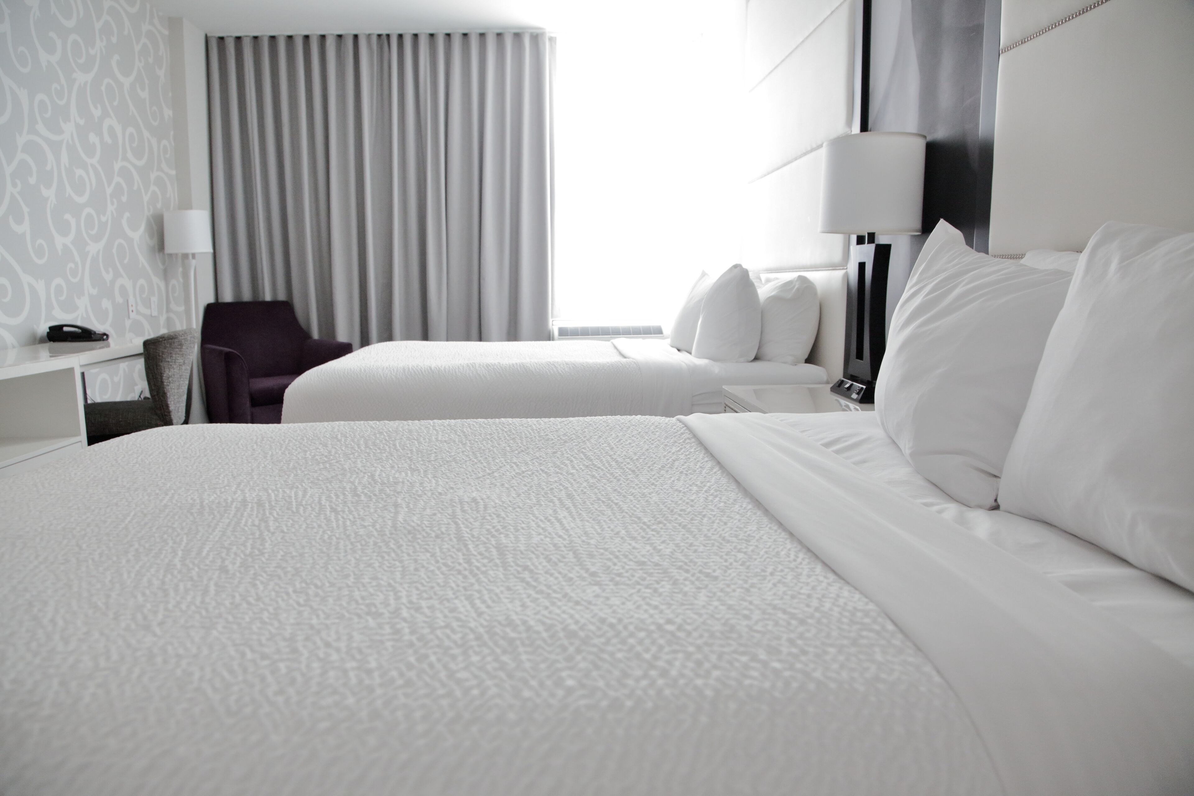 Habitación de hotel con dos camas, un escritorio con lámpara, una silla y una ventana con cortinas.