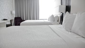 Habitación de hotel con dos camas, un escritorio con lámpara, una silla y una ventana con cortinas.