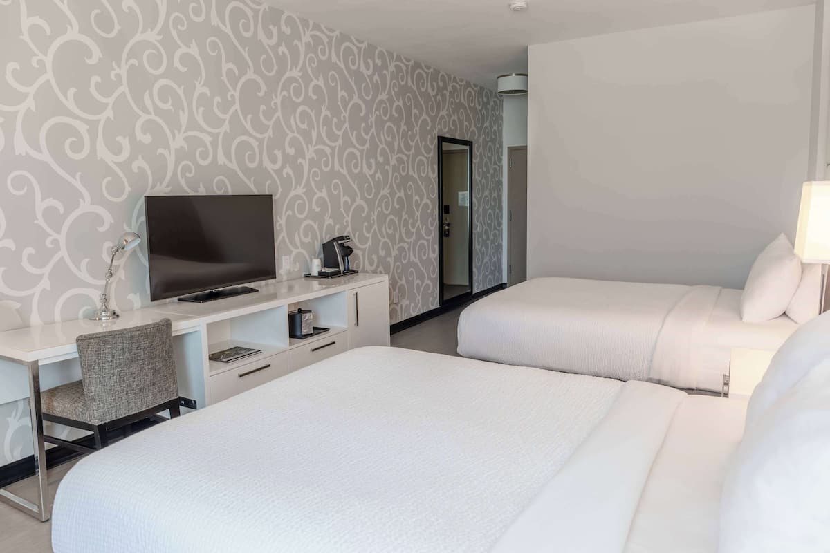 A hotel room with two beds, a desk with a TV, a chair, and a mirror.
