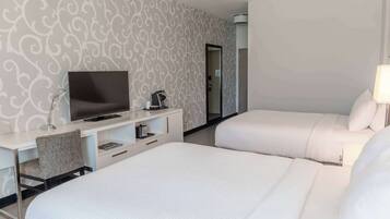 Habitación de hotel con dos camas, un escritorio, un televisor, una silla y un espejo.