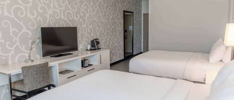 Habitación de hotel con dos camas, un escritorio, un televisor, una silla y un espejo.