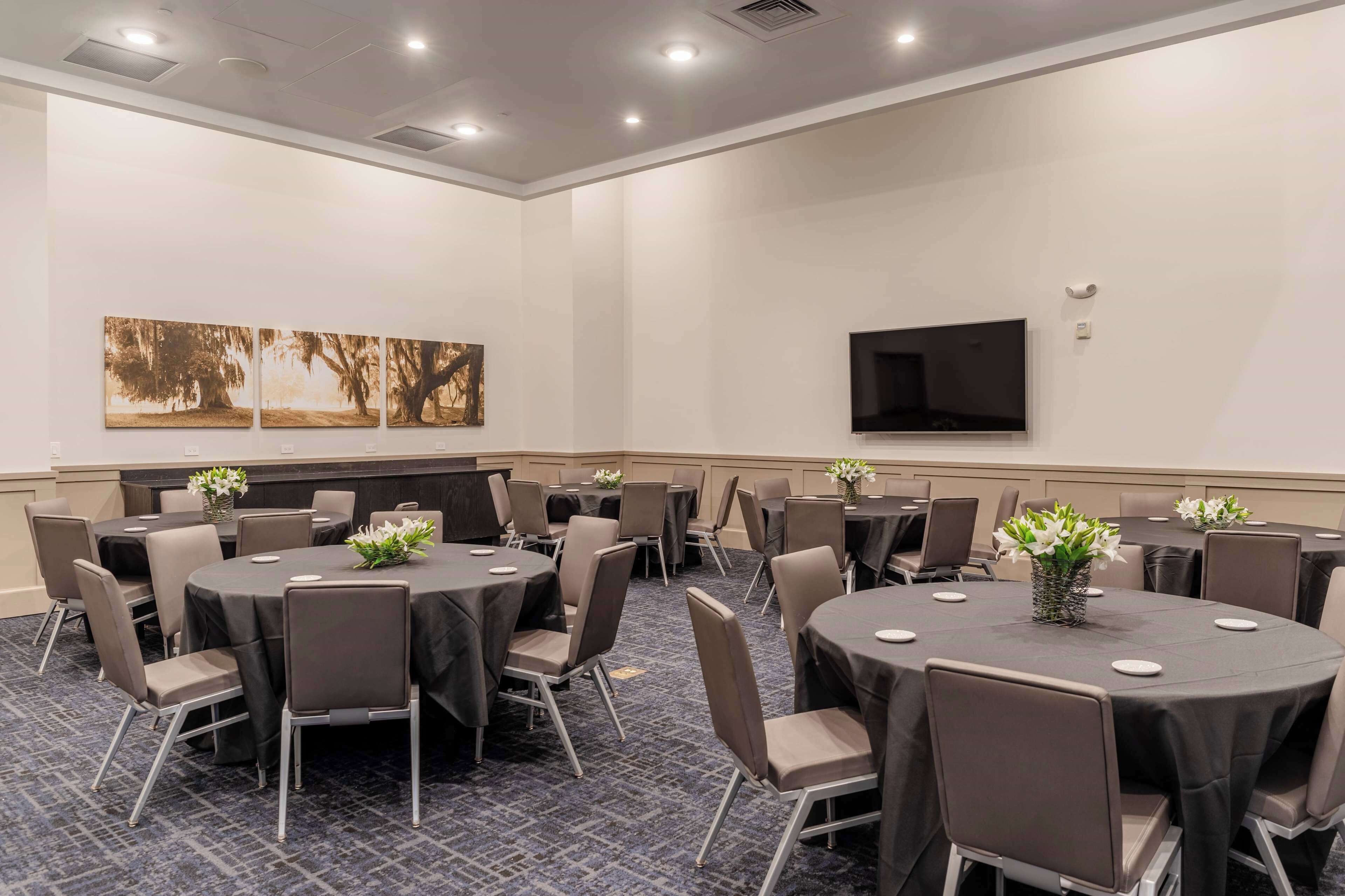 A conference room with round tables, chairs, and a flat-screen TV on the wall.