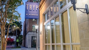 Un edificio con un cartel iluminado grande que dice "TRYP BY WYNDHAM" y una entrada bien iluminada con ventanas amplias.