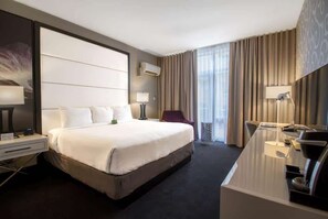 Ein modernes Hotelzimmer mit einem großen Bett, einem Schreibtisch mit Stuhl, einem kleinen Tisch und einer Lampe.