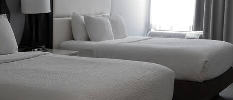 Una habitación de hotel con dos camas, una mesita de noche, una lámpara y una ventana con cortinas.