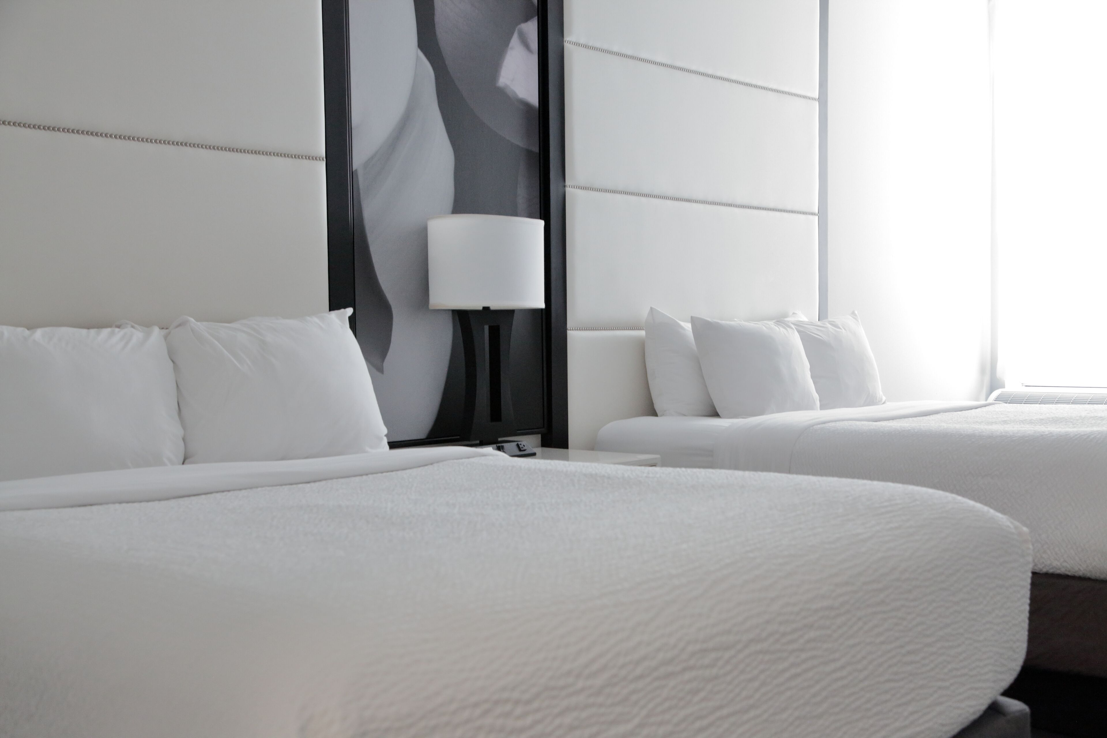 Habitación de hotel con dos camas, un ventanal grande y una lámpara fijada a la pared.
