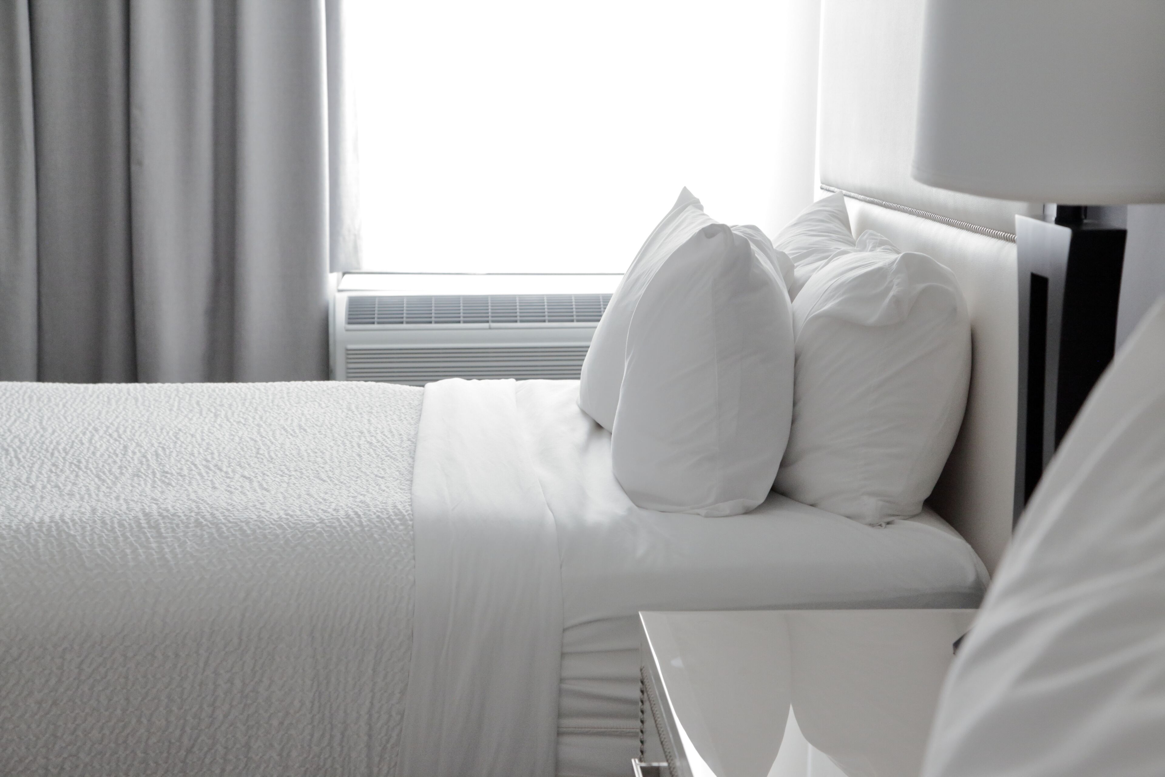 Une chambre d’hôtel avec un lit bien fait, du linge de lit blanc et une fenêtre avec des rideaux.