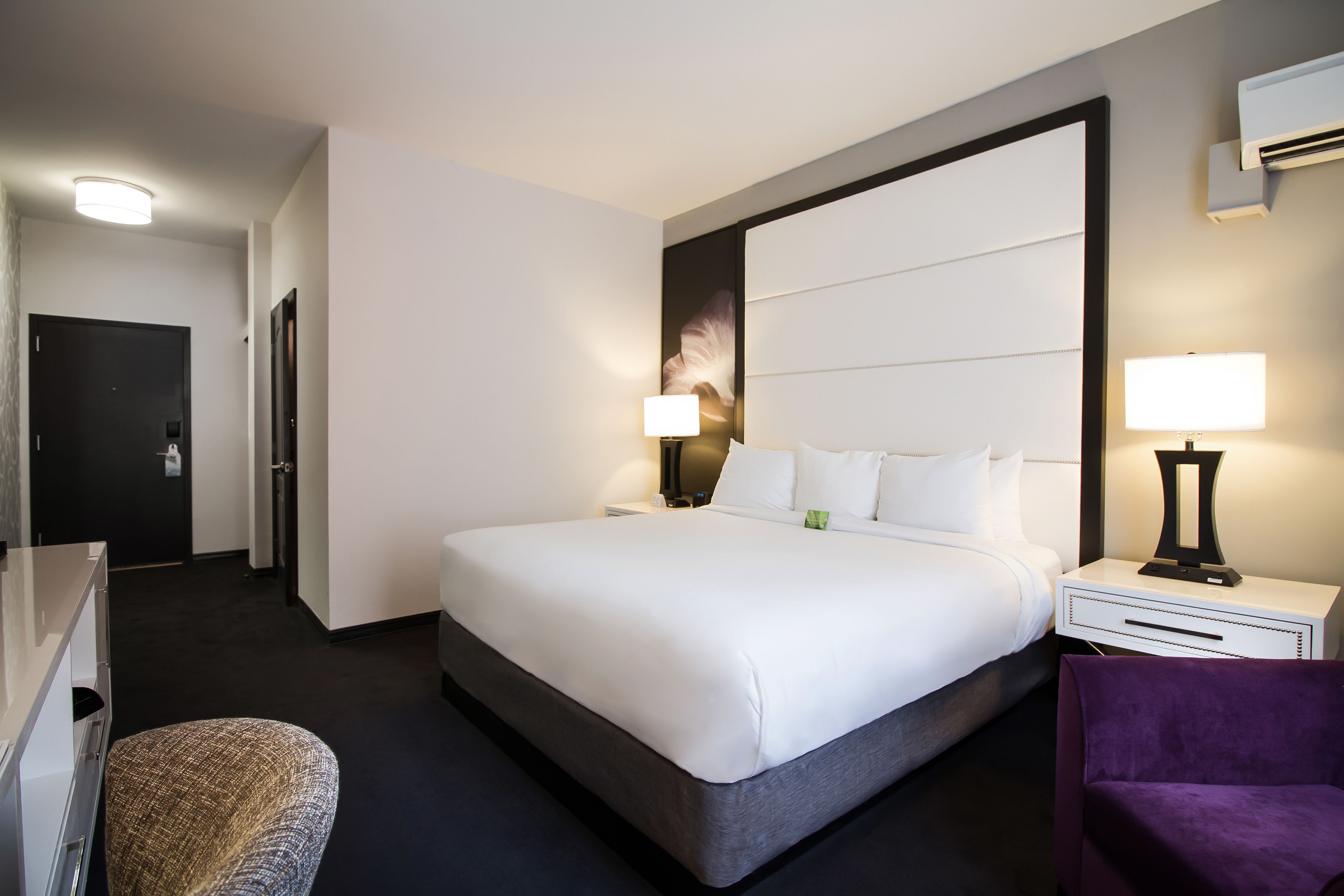 Een moderne hotelkamer met een groot bed, een nachtkastje met een lamp, een stoel en een kledingkast.