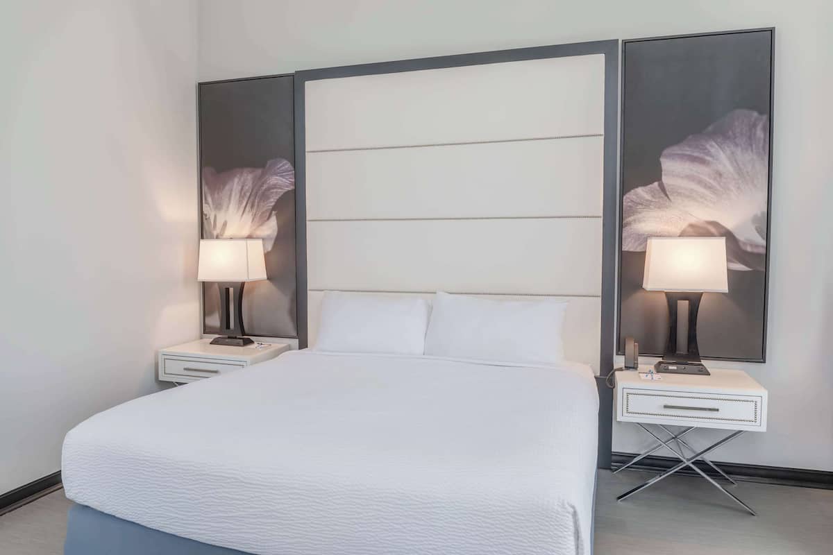 A hotel room with a large bed, two bedside tables with lamps, a nightstand, and a wall-mounted mirror.