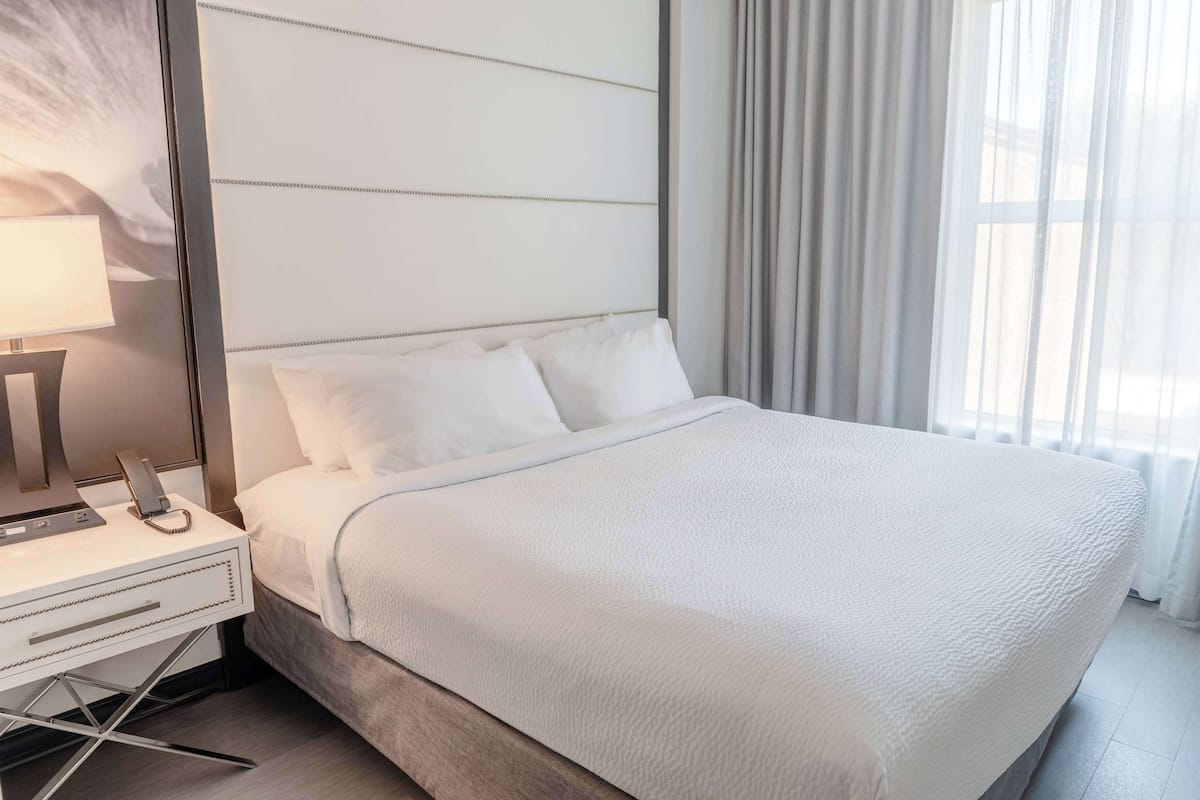 A neatly made bed with white linens, a bedside table with a lamp, and a phone.