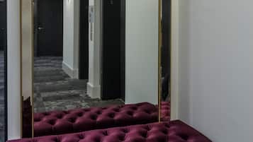 Un espejo con marco dorado, un banco tapizado y una lámpara de pared.