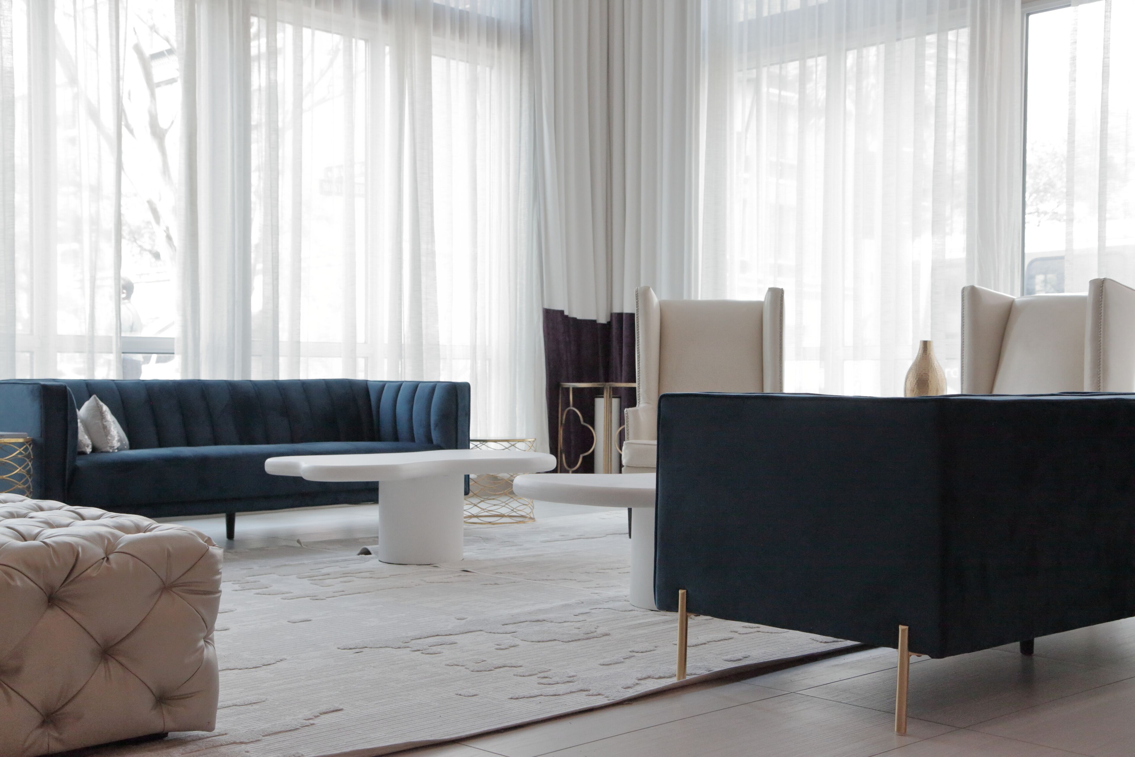 A modern living room with a dark blue sofa, a white coffee table, and a tufted ottoman.