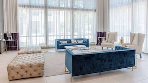 Una sala de estar moderna con un sofá azul, otomanas color beige, una mesita de centro azul oscuro y un sillón blanco.
