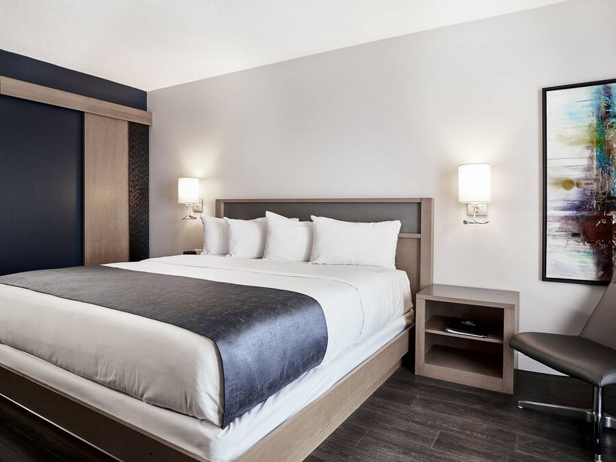 Una habitación de hotel moderna con una cama grande, mesitas de noche, una silla y un cuadro en la pared.