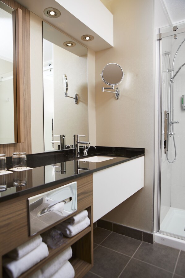 Un baño moderno con un espejo grande, un lavamanos y una ducha.