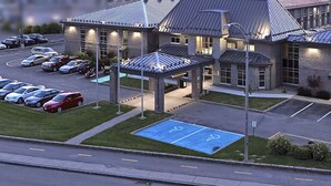 A Cofortel hotel with a parking lot, a covered parking area, and a building with a brick facade and multiple windows. - Hôtel Cofortel (L'Ancienne-Lorette)