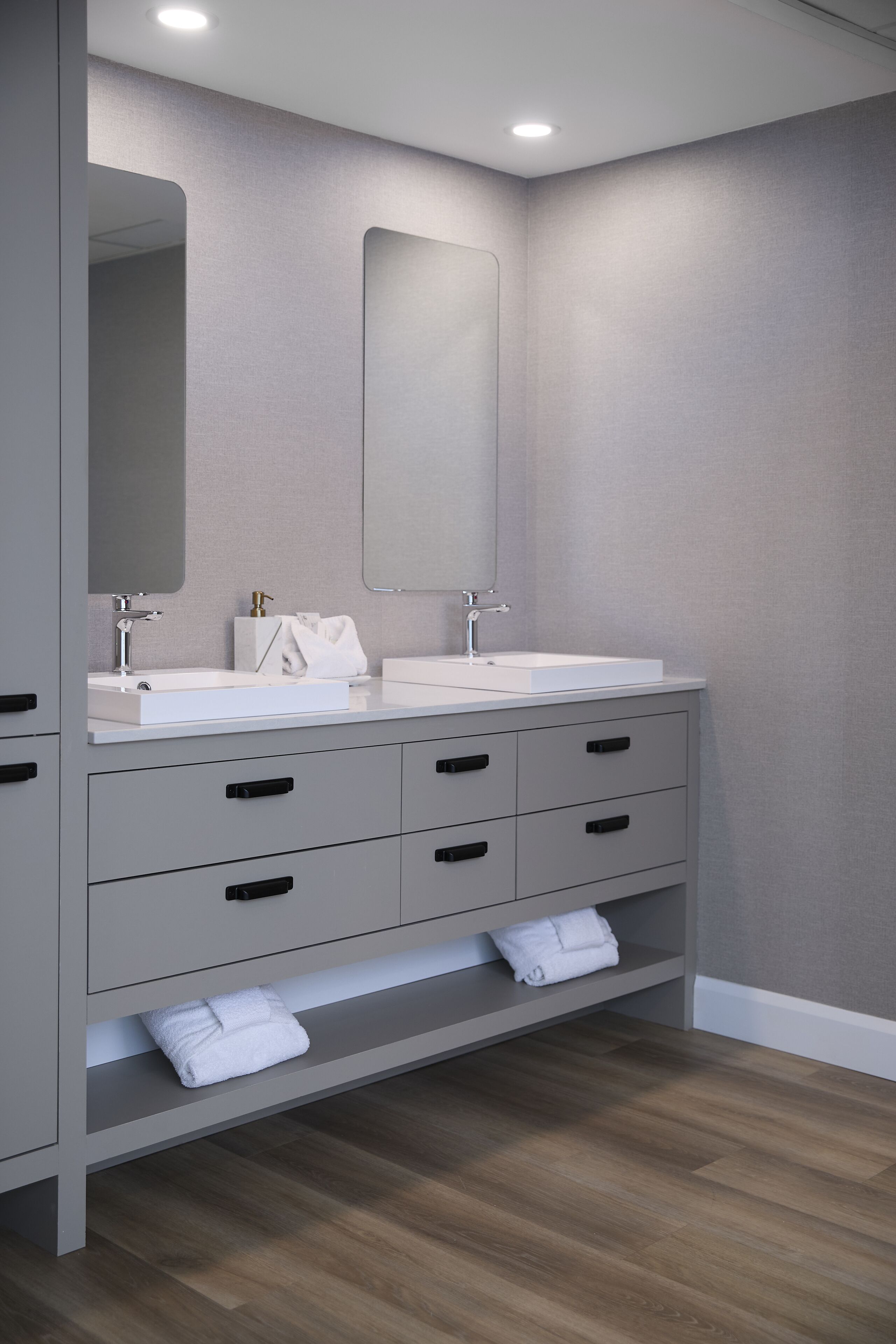 A modern bathroom with two sinks, a large mirror, and grey cabinetry.