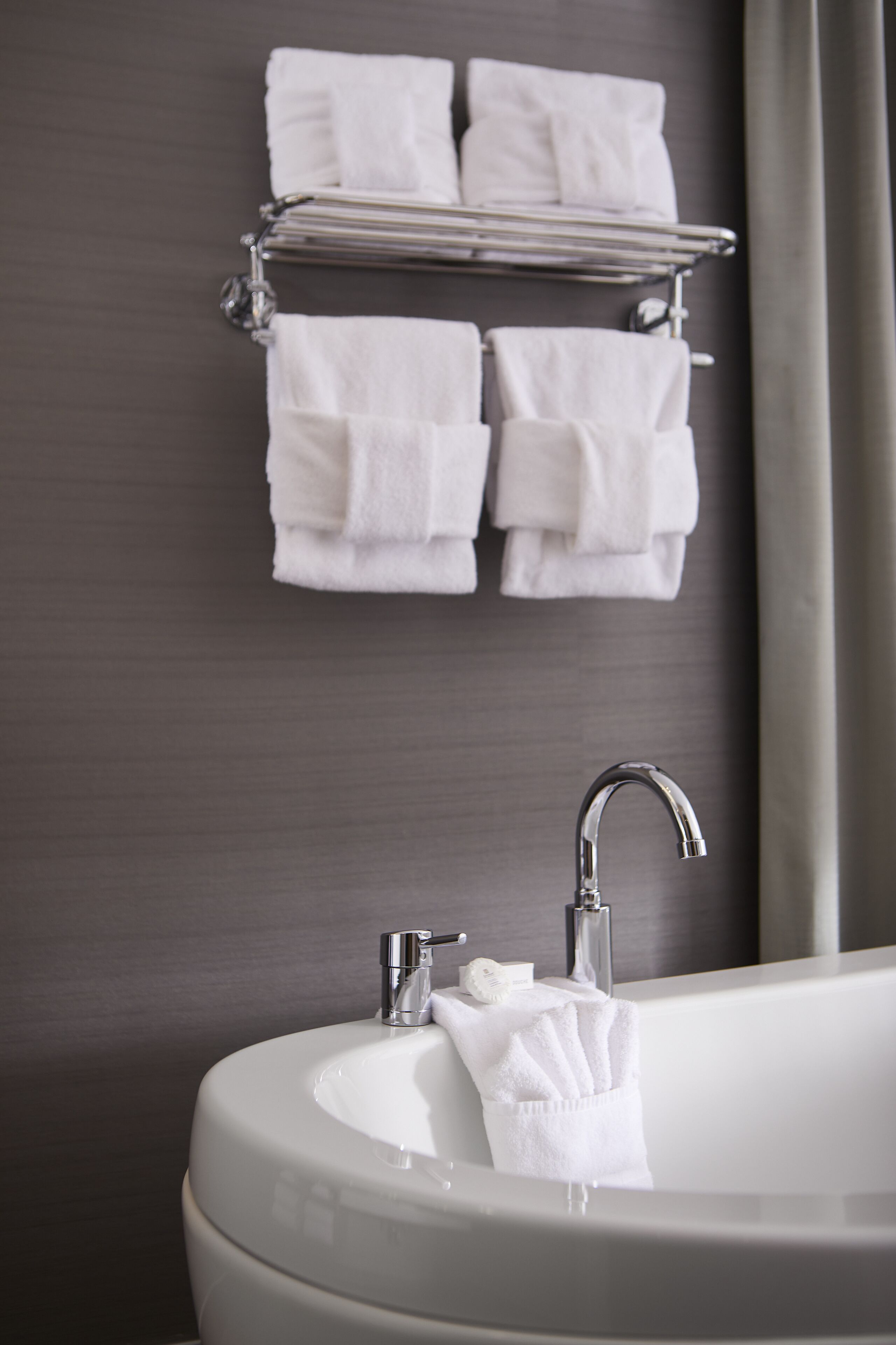 Ein Badezimmer mit einem weißen Waschbecken, einem Spiegel und einem Handtuchhalter mit mehreren Handtüchern.