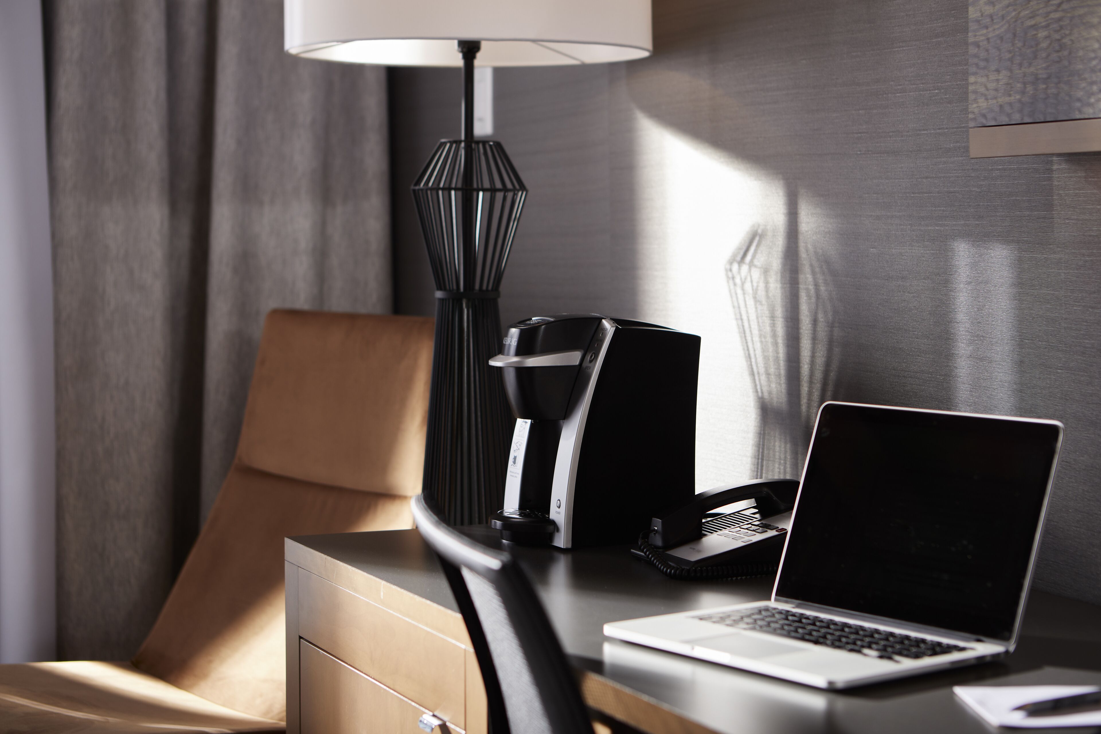 A hotel room with a desk, a laptop, a telephone, and a lamp.