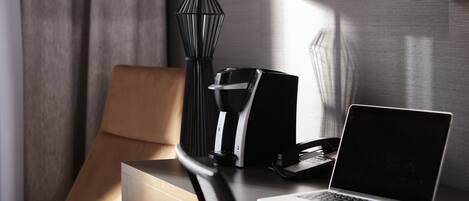 A hotel room with a desk, a laptop, a telephone, and a lamp.