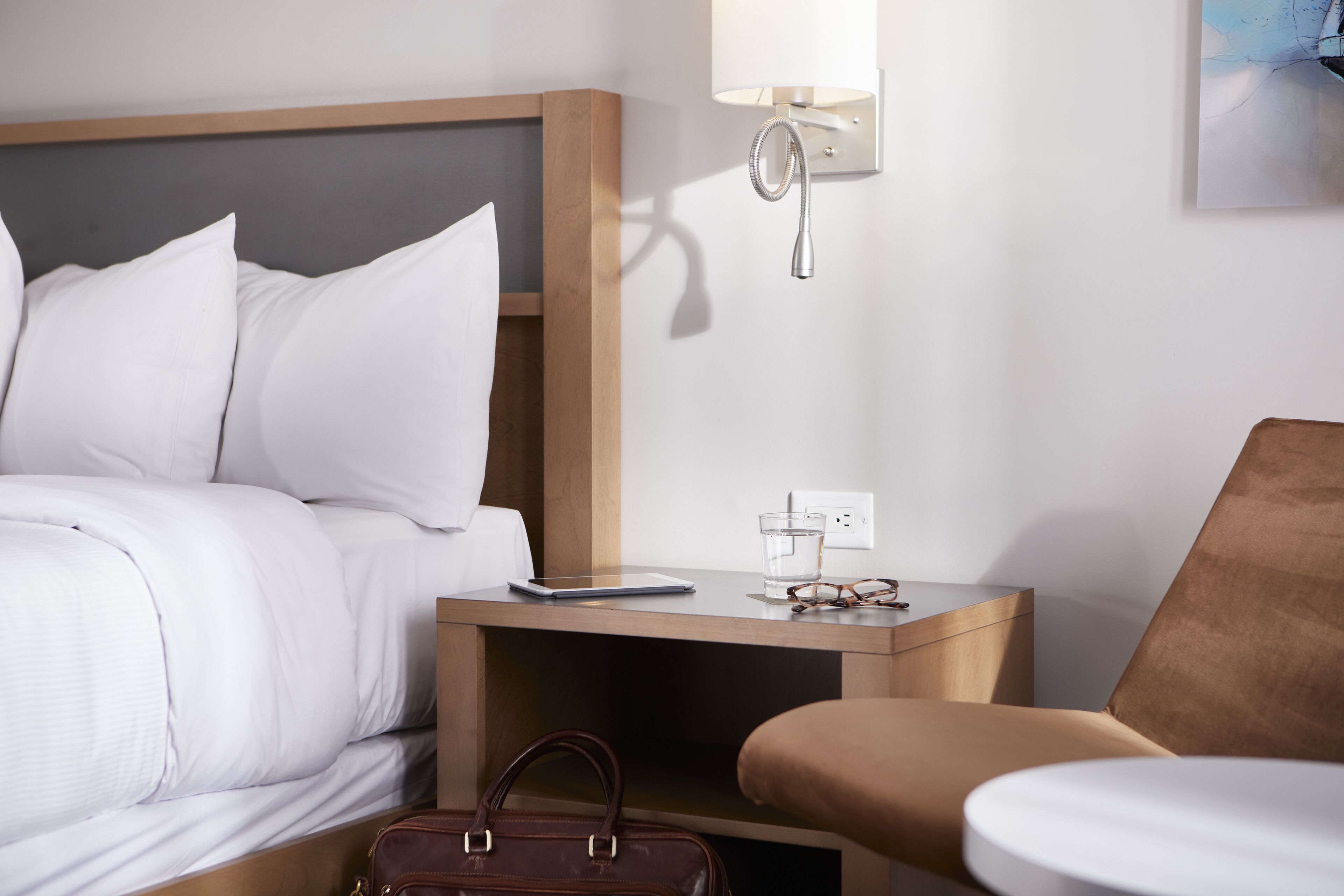 A hotel room with a bed, a nightstand with a lamp, a chair, and a suitcase.