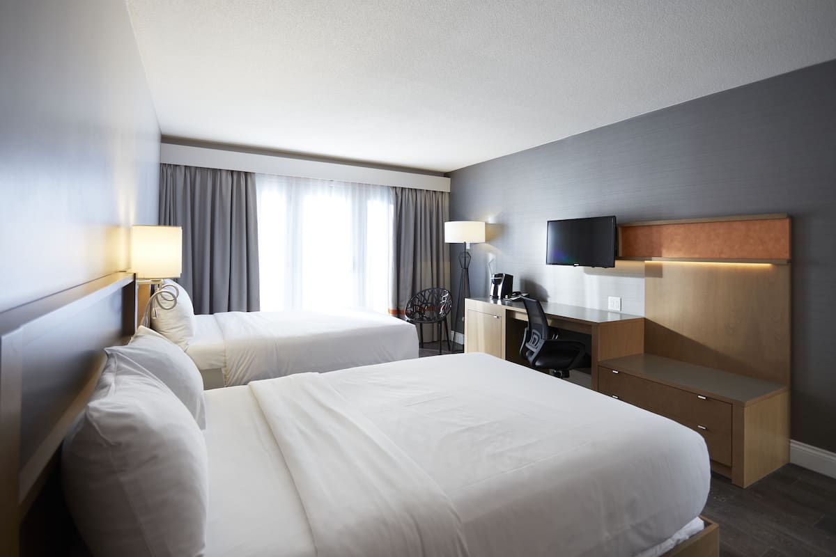 A hotel room with two beds, a desk, a chair, a TV, and a window with curtains.
