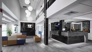 A modern reception area with a reception desk, seating area, and a large plant. - Hôtel Cofortel (L'Ancienne-Lorette)
