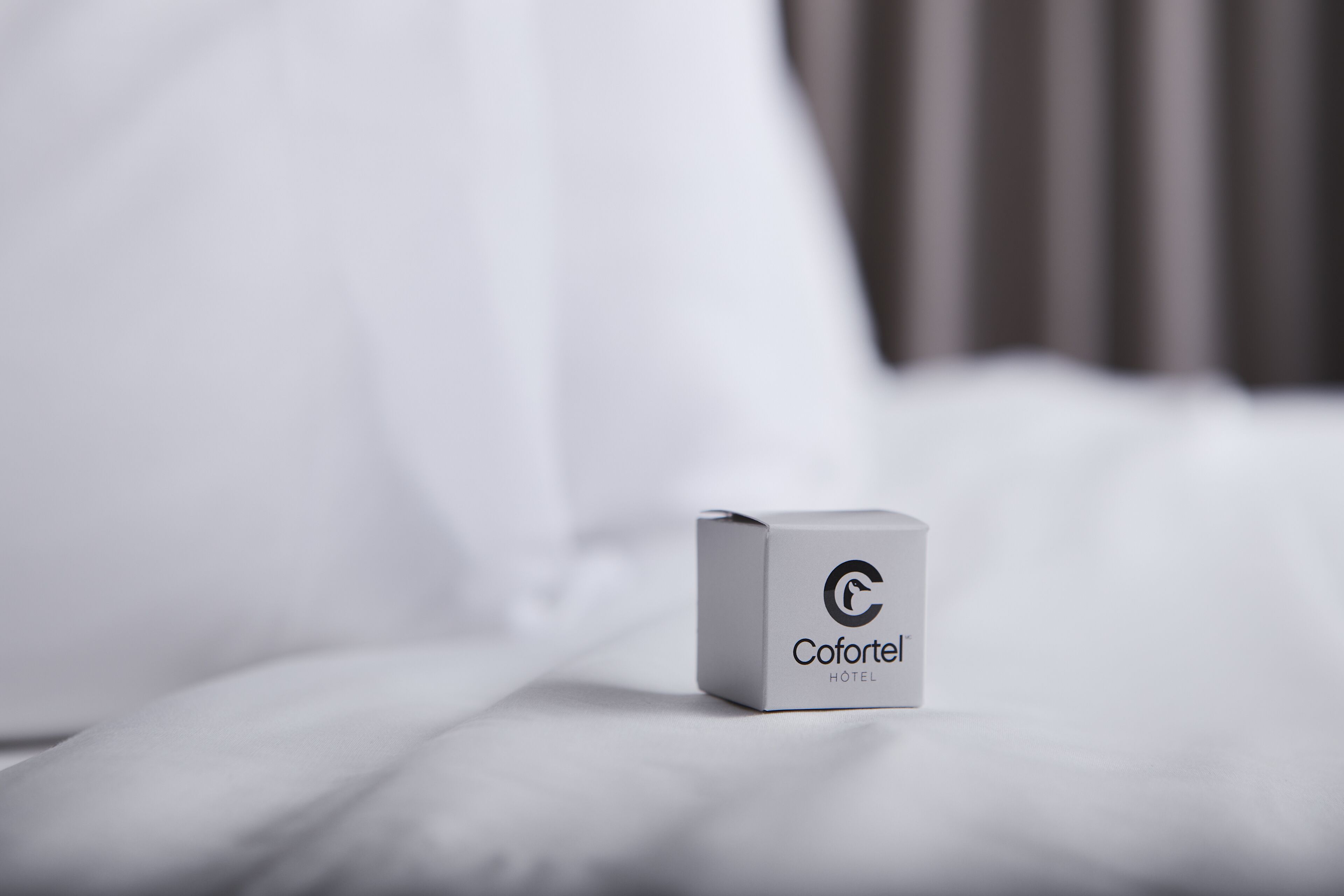 A white box with the logo and name "Coforte Hotel" on a bed.