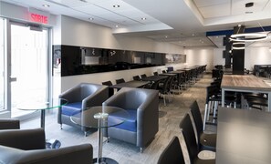 Een modern restaurant met een lange toonbank, zwarte stoelen en een glazen tafel.