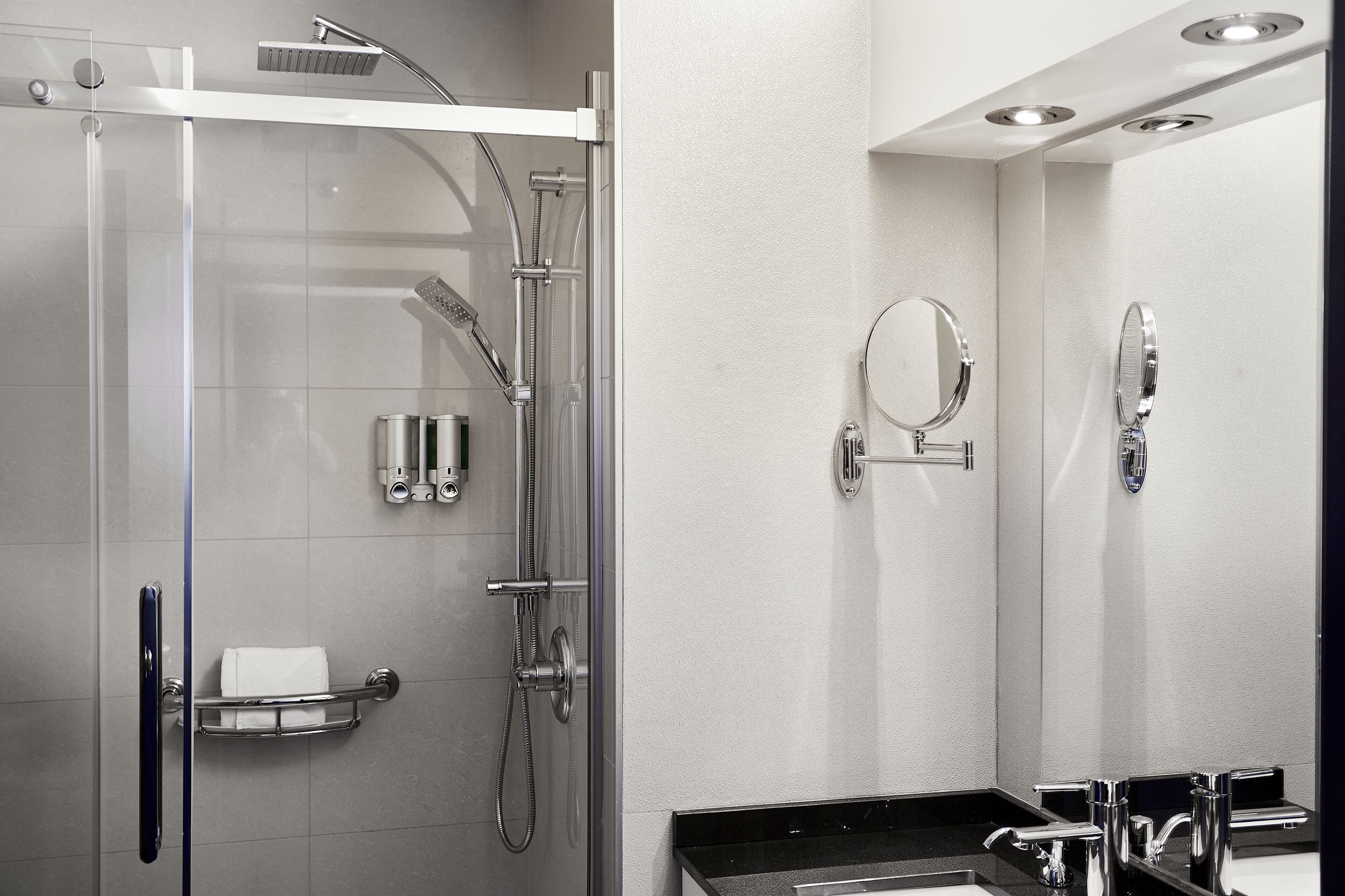 A modern bathroom with a glass-enclosed shower, a vanity with a black countertop, and two wall-mounted mirrors.