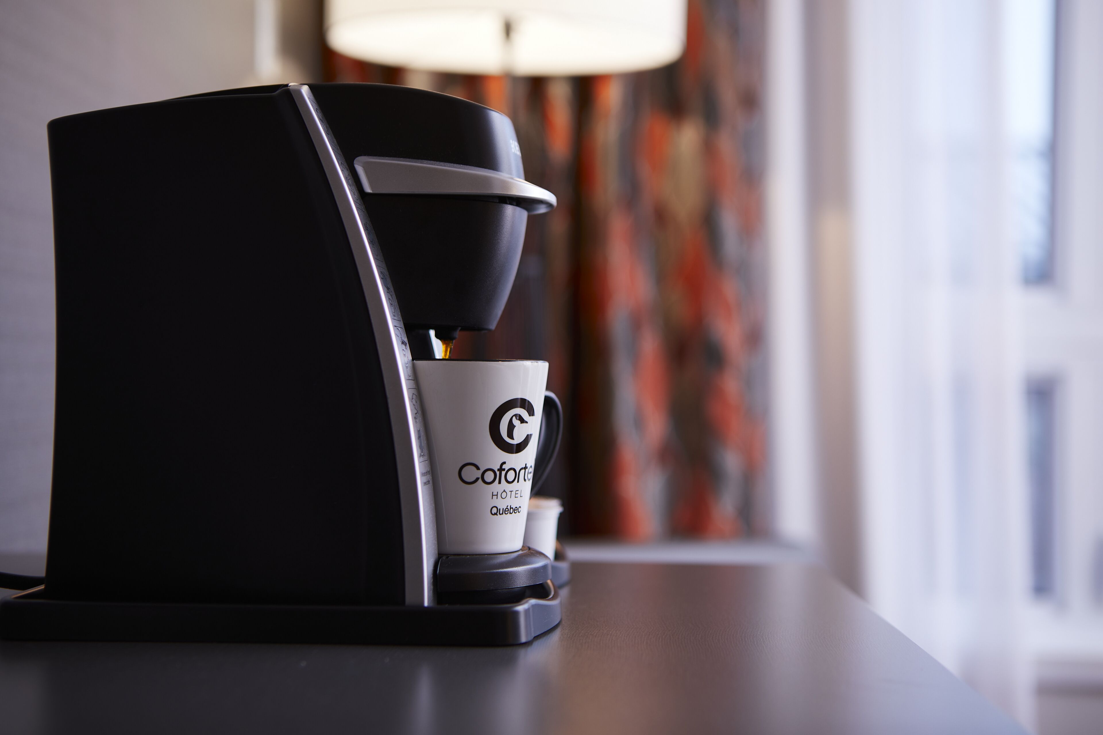 A coffee machine with a cup labeled "Coforte Hotel Quebec" on a table.