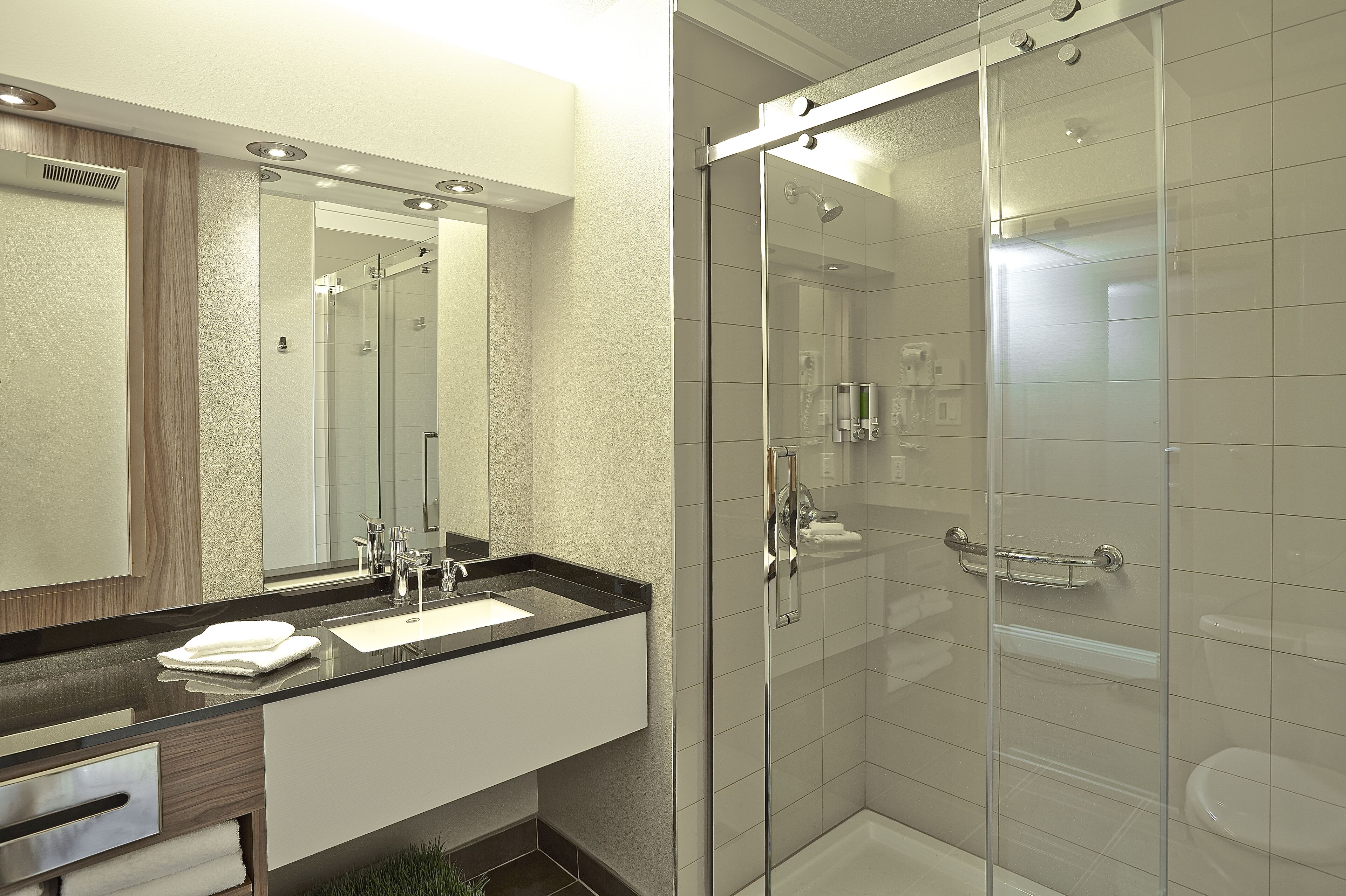 Une salle de bain moderne avec une douche à parois de verre, un grand miroir et un lavabo sur un plan de toilette noir.