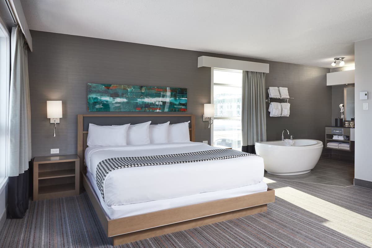 A modern hotel room with a large bed, a bathtub, and a bathroom with a mirror and towel rack.