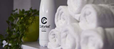 A white bottle labeled "Cofortel Hôtel Québec" and neatly rolled white towels on a white surface.